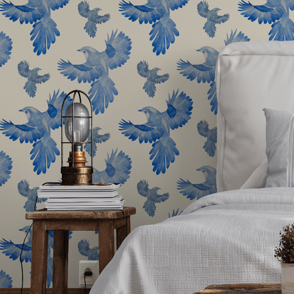 A zoomed-in azure blue birds in flight peel and stick wallpaper behind rustic wooden side table and soft grey bedding in cozy bedroom