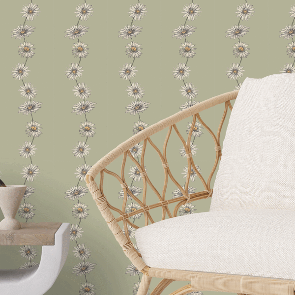 Zoomed-in of Ditzy Daisy Chain peel and stick wallpaper in taupe and ivory floral garlands on a soft sage green background behind a rattan chair with cream cushion