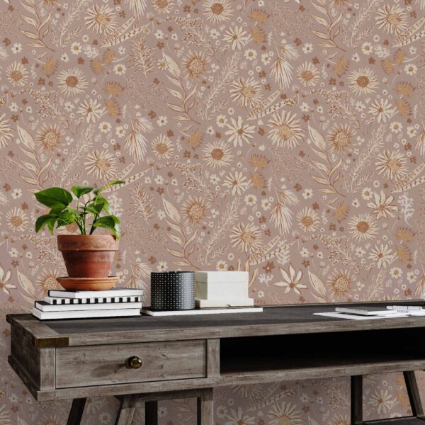A zoomed-in boho floral wallpaper in blush pink and gold behind a rustic wood desk and antique chair in a cozy home office