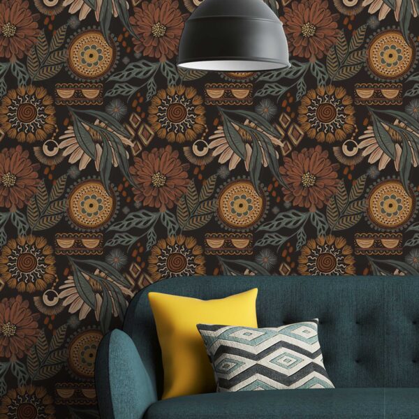 A zoomed-in Boho Bliss bohemian wallpaper featuring ochre and terracotta flowers with tribal sun and moon elements behind a teal sofa with yellow cushion