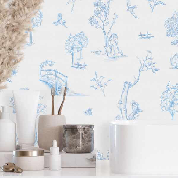 Forest Toile in Blue peel and stick wallpaper behind a modern bathroom sink with black faucet and neutral decor accents