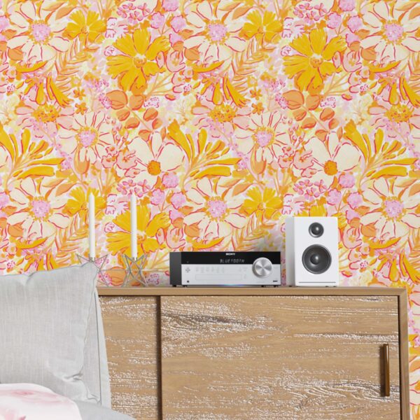 A zoomed-in vibrant floral wallpaper in shades of yellow, orange, and pink behind a modern grey sofa and wooden sideboard
