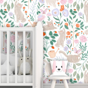 Purrfect Garden peel and stick wallpaper featuring playful beige cats, strawberries, butterflies, and wildflowers behind a white crib and oversized plush toys in a colourful playroom