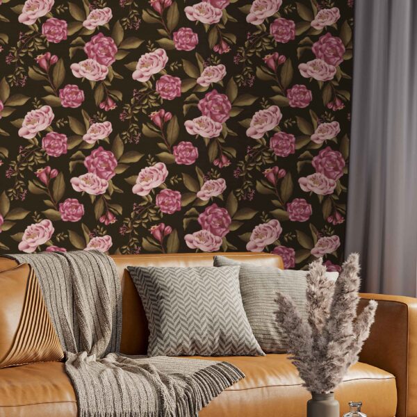 A zoomed-in Victorian Blooms Dark peel and stick wallpaper with rich pink roses and olive foliage on a deep brown-black background behind a caramel leather sofa