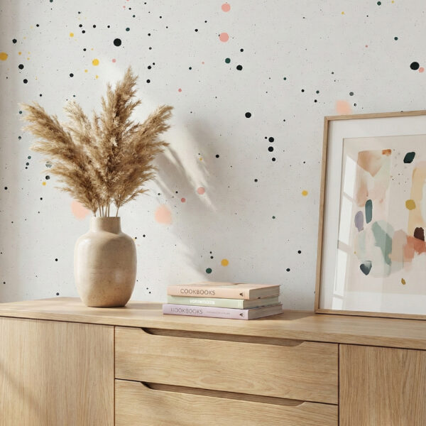 A zoomed-in of confetti dot wallpaper styled above a light wood sideboard with ceramic vase, framed artwork, and neutral decor