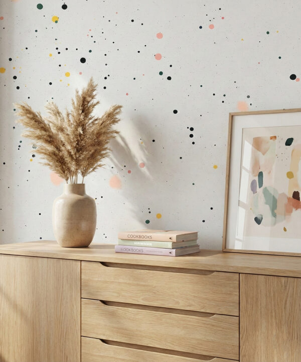 A zoomed-in of confetti dot wallpaper styled above a light wood sideboard with ceramic vase, framed artwork, and neutral decor