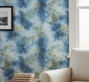 A zoomed in of Azure Mist wallpaper displayed in a living room with a white armchair, framed artwork, and painterly blue forest pattern.