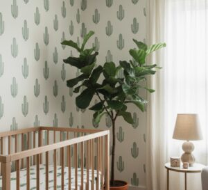 A zoom in of sage cactus wallpaper detail behind a wooden crib and leafy indoor plant in a calm, modern nursery.