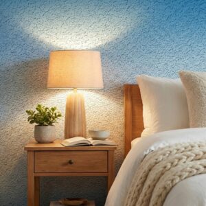 A zoomed-in of sapphire ombre wallpaper in a bedroom with bedside table, lamp, and neutral linens.