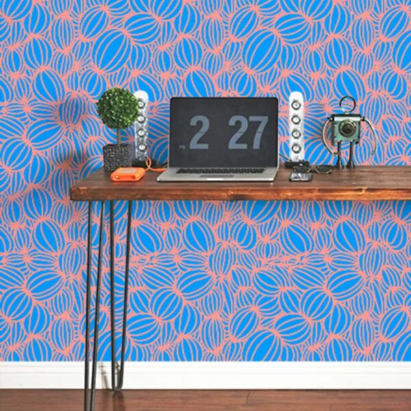 A zoomed-in of we’re All Connected wallpaper with coral looping lines forming organic shapes on a bright blue background behind a desk.