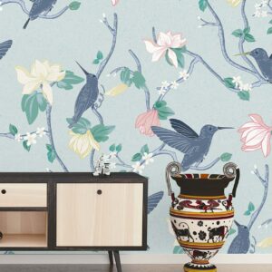 Guilded Fusion Chinoiserie Blue Heron wallpaper in a styled living room with hummingbirds, floral branches, and soft blue background.