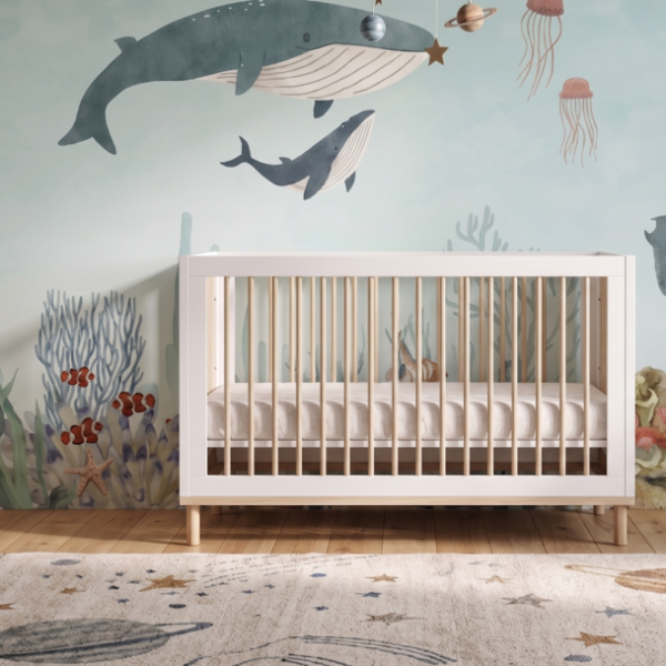 A nursery featuring the Ocean Wonders Mural with whales and underwater sea life behind a white crib.